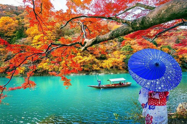 mujer vestida tradicionalmente junto al río en Kioto con colores de otoño