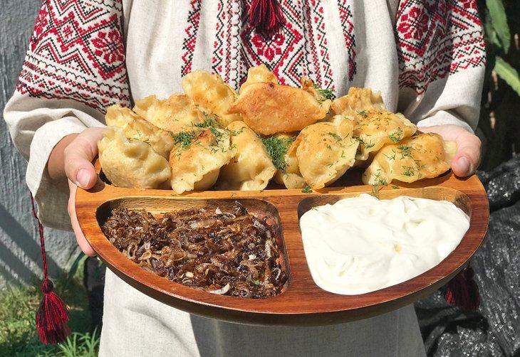Femme ukrainienne tenant une assiette de vareniki (raviolis) avec des oignons frits et de la crème aigre.