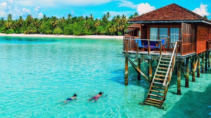Couple faisant de la plongée avec tuba à côté d'un bungalow au bord de l'eau aux Maldives